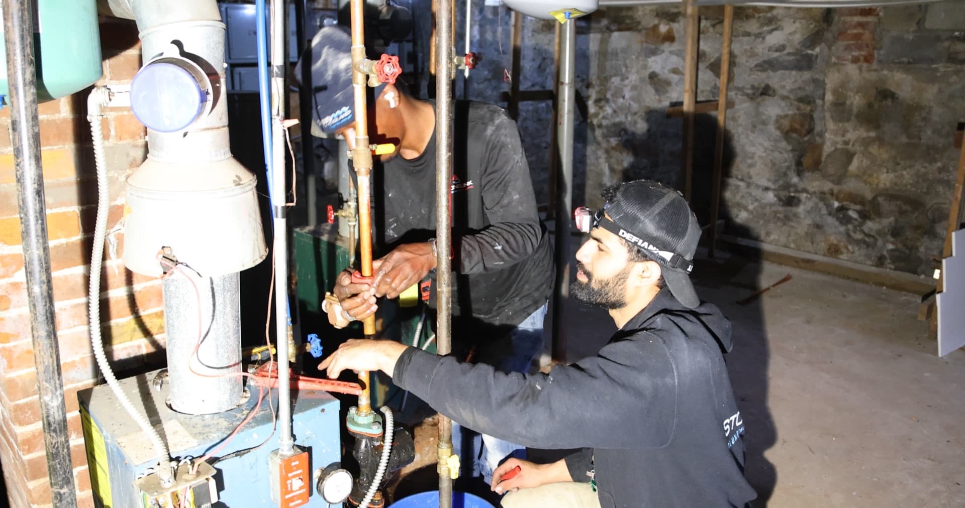 Professional plumbers working on copper pipes in basement